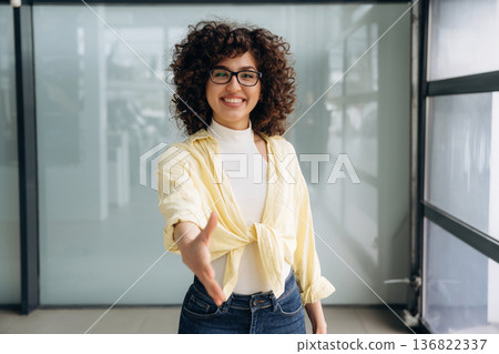 Giving hand to shake. Beautiful woman is standing indoors against blurred wall Giving hand to shake. Beautiful woman is standing indoors against blurred wall 136822337
