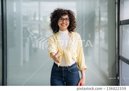 Giving hand to shake. Beautiful woman is standing indoors against blurred wall Giving hand to shake. Beautiful woman is standing indoors against blurred wall 136822339