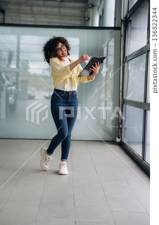 Writing the information while talking by the phone. Beautiful woman is standing indoors against blurred wall Writing the information while talking by the phone. Beautiful woman is standing indoors against blurred wall 136822344