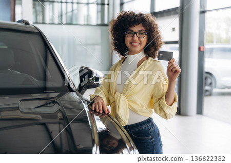 In casual clothes, standing by the vehicle. Pretty woman is in the car retail shop In casual clothes, standing by the vehicle. Pretty woman is in the car retail shop 136822382