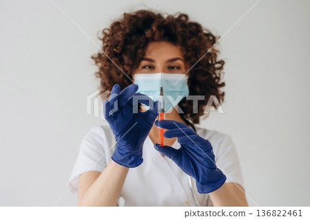 Syringe with red orange color liquid. Beautiful doctor woman is in the studio Syringe with red orange color liquid. Beautiful doctor woman is in the studio 136822461