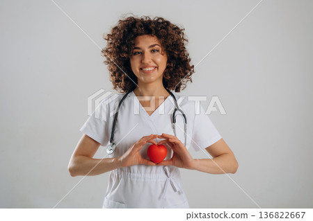 Cardiologist is with little heart toy. Beautiful doctor woman is in the studio 136822667