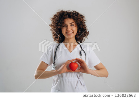 Cardiologist is with little heart toy. Beautiful doctor woman is in the studio 136822668