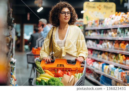 Fruits and vegetables in the cart. Gorgeous woman is in the grocery store Fruits and vegetables in the cart. Gorgeous woman is in the grocery store 136823431