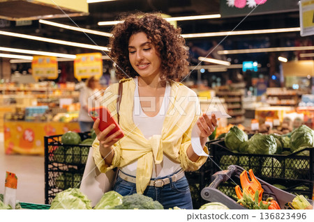 Red smartphone is in hand. Gorgeous woman is in the grocery store Red smartphone is in hand. Gorgeous woman is in the grocery store 136823496