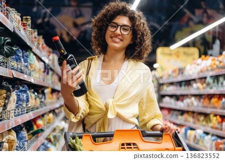 Bottle is in hands. Gorgeous woman is in the grocery store 136823552