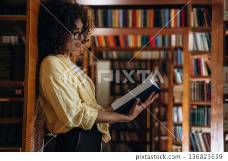 Leaning on the shelf. Beautiful woman is in the library Leaning on the shelf. Beautiful woman is in the library 136823659