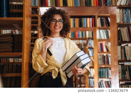 Bunch of books are in hands. Beautiful woman is in the library Bunch of books are in hands. Beautiful woman is in the library 136823674