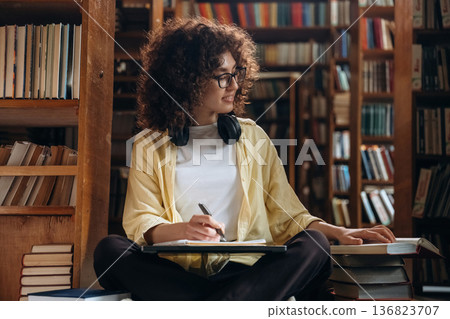 The writing process. With pen and headphones. Beautiful woman is in the library The writing process. With pen and headphones. Beautiful woman is in the library 136823707