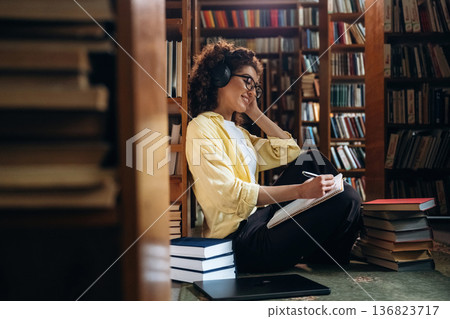 Listening to music and writing. Beautiful woman is in the library Listening to music and writing. Beautiful woman is in the library 136823717
