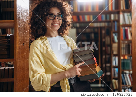 Colorful covers on books. Holding them. Beautiful woman is in the library Colorful covers on books. Holding them. Beautiful woman is in the library 136823725