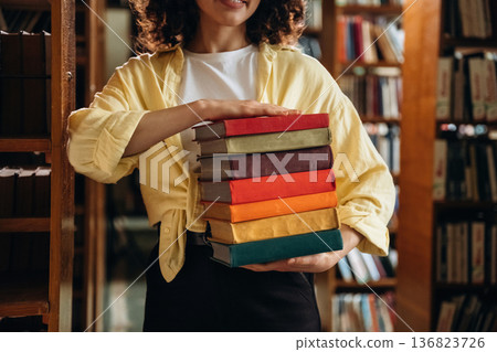 Colorful covers on books. Holding them. Beautiful woman is in the library Colorful covers on books. Holding them. Beautiful woman is in the library 136823726