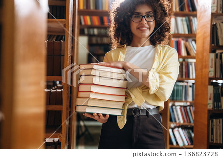 That's a lot of books in hands. Beautiful woman is in the library That's a lot of books in hands. Beautiful woman is in the library 136823728