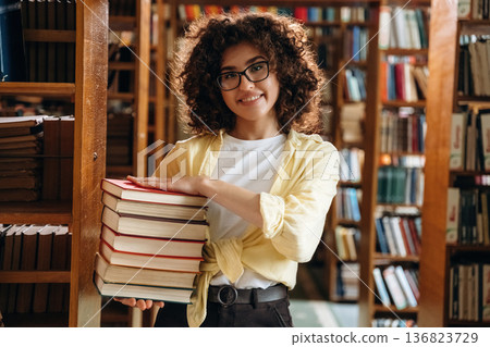 That's a lot of books in hands. Beautiful woman is in the library That's a lot of books in hands. Beautiful woman is in the library 136823729