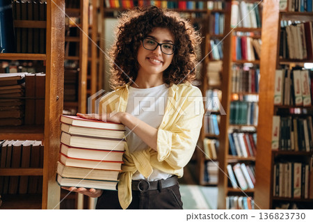That's a lot of books in hands. Beautiful woman is in the library 136823730
