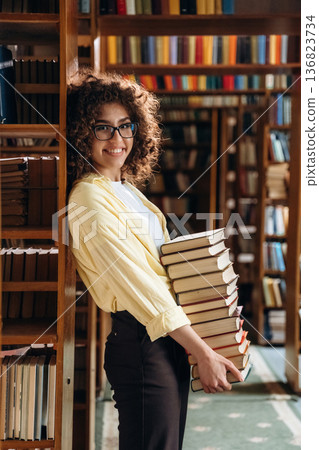 That's a lot of books in hands. Beautiful woman is in the library That's a lot of books in hands. Beautiful woman is in the library 136823734