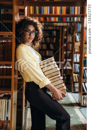 View from the side, holding lot of books. Beautiful woman is in the library View from the side, holding lot of books. Beautiful woman is in the library 136823735