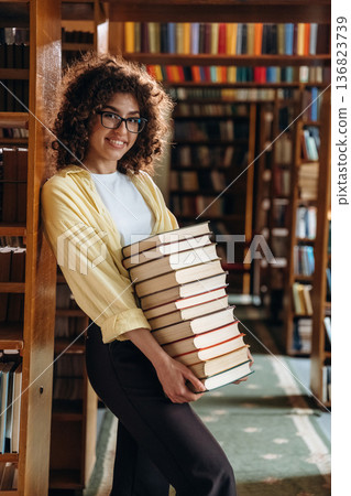 View from the side, holding lot of books. Beautiful woman is in the library 136823739