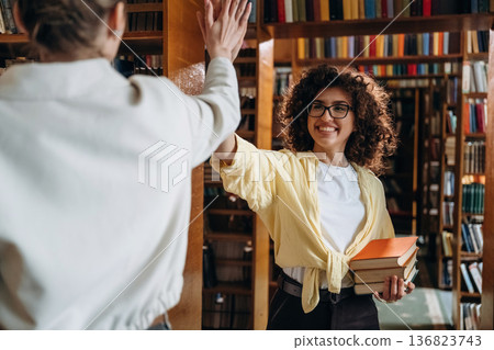 Two women are doing high five in the library Two women are doing high five in the library 136823743