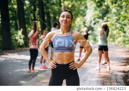 Abs, strong fitness woman is standing. Group of runners are together outdoors Abs, strong fitness woman is standing. Group of runners are together outdoors 136824223