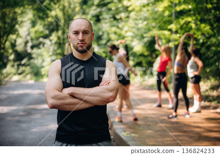 Man is standing in front of people. Group of runners are together outdoors Man is standing in front of people. Group of runners are together outdoors 136824233