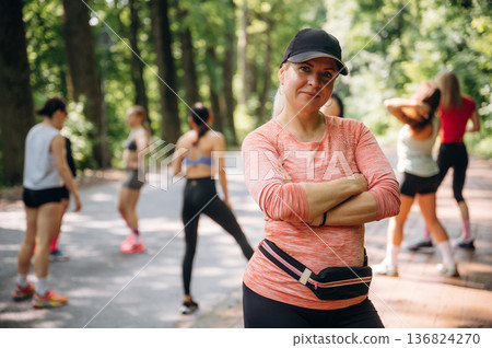With arms crossed, woman is standing. Group of runners are together outdoors 136824270
