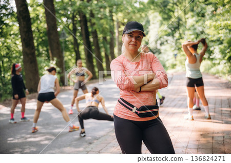 With arms crossed, woman is standing. Group of runners are together outdoors 136824271