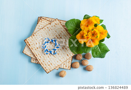 Passover holiday card with matzah, walnuts, yellow spring flowers on light blue background, gold and white accents, copy space 136824489