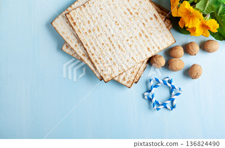 Passover holiday card with matzah, walnuts, yellow spring flowers on light blue background, gold and white accents, copy space 136824490