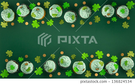 St. Patrick's Day vanilla and chocolate cupcakes with green frosting and  shiny clover decorations on green paper background. Irish holiday dessert concept. Top view, copy space. 136824534