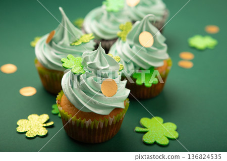 St. Patrick's Day vanilla cupcakes with green frosting and  shiny clover decorations on green paper background. Irish holiday dessert concept, copy space. 136824535