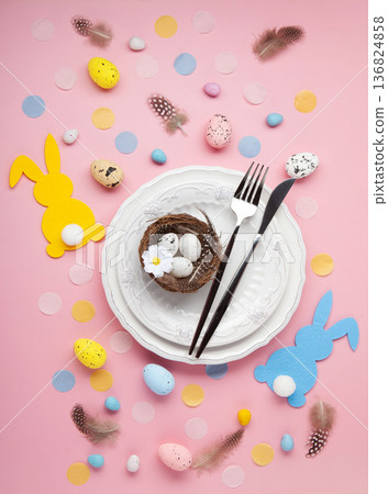 Easter spring holiday table setting. White plate, cutlery, soft bunny, painted eggs, spring flowers on light pink background. Festive dining scene 136824858