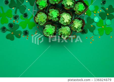 St. Patrick's Day vanilla cupcakes with green frosting and clover decorations on green background. Irish holiday dessert concept. Top view, copy space St. Patrick's Day vanilla cupcakes with green frosting and clover decorations on green background. Irish holiday dessert concept. Top view, copy space 136824879