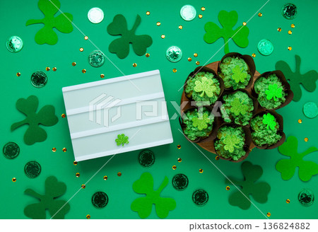 St. Patrick's Day vanilla cupcakes with green frosting and clover decorations on green background. Irish holiday dessert concept. Top view, copy space St. Patrick's Day vanilla cupcakes with green frosting and clover decorations on green background. Irish holiday dessert concept. Top view, copy space 136824882