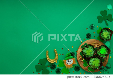 St. Patrick's Day vanilla cupcakes with green frosting and clover decorations on green background. Irish holiday dessert concept. Top view, copy space 136824893