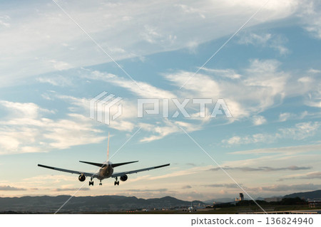 A passenger plane landing in the evening sky and a serene mountain range 136824940