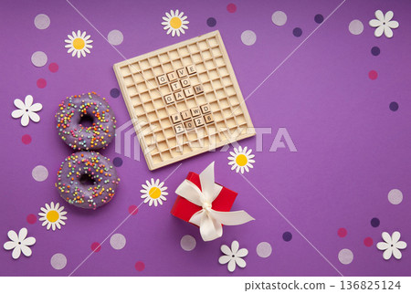 Give to Gain concept for International Women's Day, 8 march. Two purple doughnuts, red gift box and spring flowers, top view flat lay Give to Gain concept for International Women's Day, 8 march. Two purple doughnuts, red gift box and spring flowers, top view flat lay 136825124