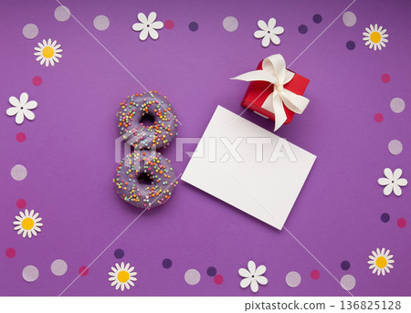 Give to Gain concept for International Women's Day, 8 march. Two purple doughnuts, red gift box and spring flowers, top view flat lay Give to Gain concept for International Women's Day, 8 march. Two purple doughnuts, red gift box and spring flowers, top view flat lay 136825128