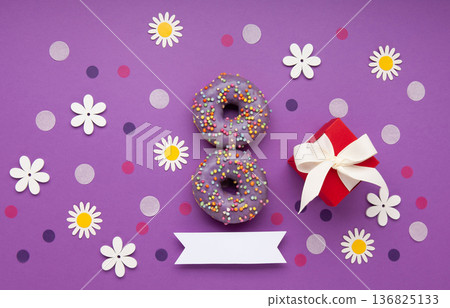 Give to Gain concept for International Women's Day, 8 march. Two purple doughnuts, red gift box and spring flowers, top view flat lay Give to Gain concept for International Women's Day, 8 march. Two purple doughnuts, red gift box and spring flowers, top view flat lay 136825133