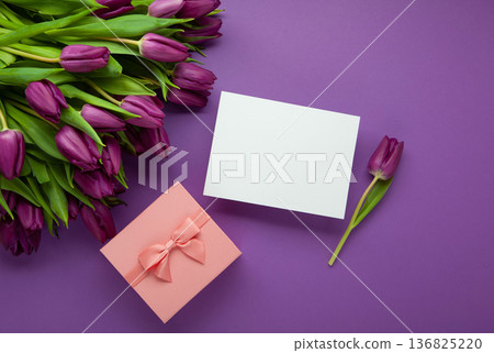 Holiday gift with pink ribbon bow, bouquet of purple tulips flower on purple background. Happy Mother's Day spring design. Holiday gift with pink ribbon bow, bouquet of purple tulips flower on purple background. Happy Mother's Day spring design. 136825220