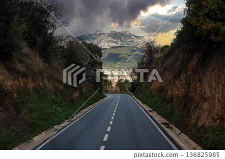 Road leading towards mountain peaks under a dramatic sky with sunlight rays, perfect for travel, adventure, and journey concepts Road leading towards mountain peaks under a dramatic sky with sunlight rays, perfect for travel, adventure, and journey concepts 136825985