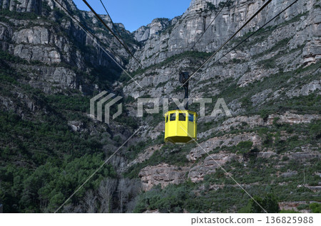 Iconic yellow Aeri de Montserrat cable car ascending the rugged jagged peaks of Montserrat mountain in Catalonia, Spain, under a clear blue sky 136825988