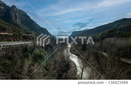 landscape of Llobregat River flowing through the valley of Montserrat mountains under a scenic sky with lush nature and rugged cliffs 136825989