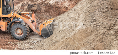 A powerful loader carefully maneuvers to move sand at a construction site. The operator skillfully plans the shifting of materials, showcasing precision 136826182