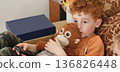 A cute boy with curly red hair is holding a stuffed monkey and looking sad 136826448