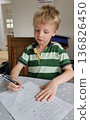 A boy is writing on a piece of paper with a pen 136826450