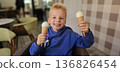 Smiling young boy is holding two ice cream cones. He is smiling and he is enjoying his treat. 136826454