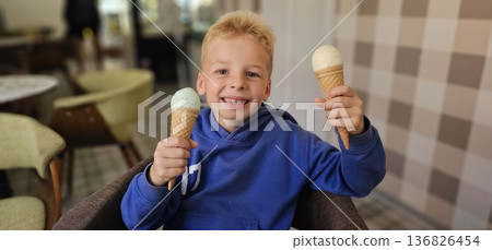 Smiling young boy is holding two ice cream cones. He is smiling and he is enjoying his treat. Smiling young boy is holding two ice cream cones. He is smiling and he is enjoying his treat. 136826454