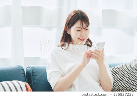 一位30多歲的女性在家中客廳使用智慧型手機的生活方式 136827222