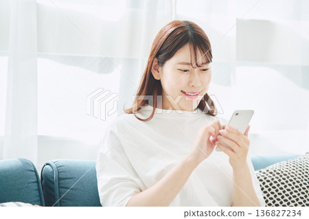 一位30多歲的女性在家中客廳使用智慧型手機的生活方式 136827234